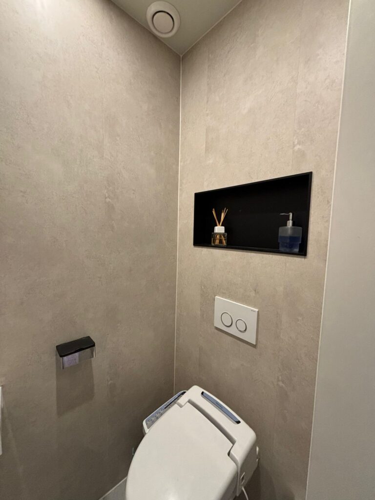 Gerenoveerde toiletruimte met lichte wandpanelen en een nis boven het wandcloset